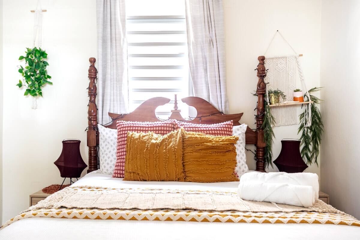 A neatly made bed with a wooden headboard, a macrame wall hanging, and a small plant on the nightstand.