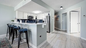 Moderni keittiö, jossa on keskeinen keittiösaareke, baarituolit, jääkaappi ja mikroaaltouuni.