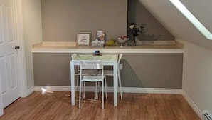 A small room with a white table and chair, a framed picture, and a vase with flowers on the wall. - Happy Moose Guest Suite (Lake Echo)