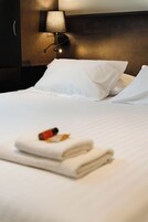 Una cama bien hecha con sábanas y almohadas blancas, una toalla doblada y una botella de loción sobre la cama.
