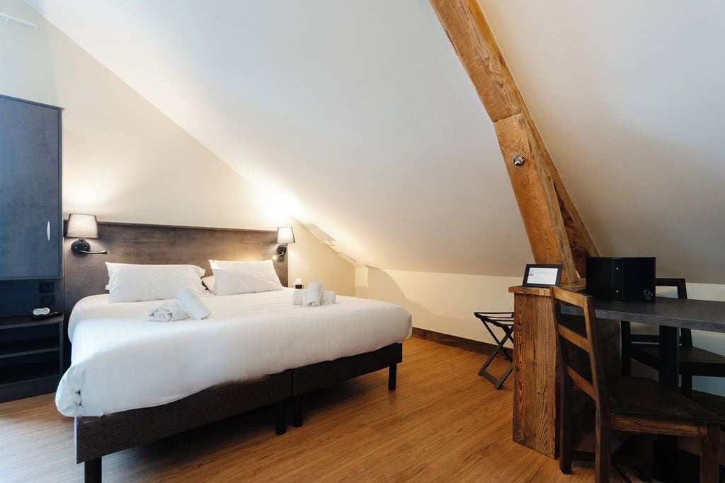 A modern bedroom with a large bed, wooden ceiling beams, and a desk with a chair.