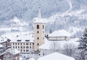 A snow-covered town with a prominent tower building, surrounded by residential buildings and a forested mountain backdrop. - Hostellerie du petit Saint Bernard (Bourg-Saint-Maurice)