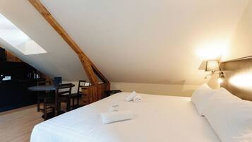A bedroom with a sloped ceiling, a bed with white linens, a desk with a chair, and a lamp on the wall.
