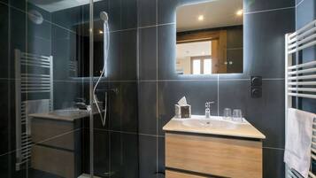 Un baño moderno con ducha de vidrio, tocador con espejo y perchero para toallas.