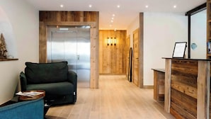 Un interior moderno con un muro decorativo de madera, un sofá, una mesita y una zona de cocina con un refrigerador y un mueble de madera.