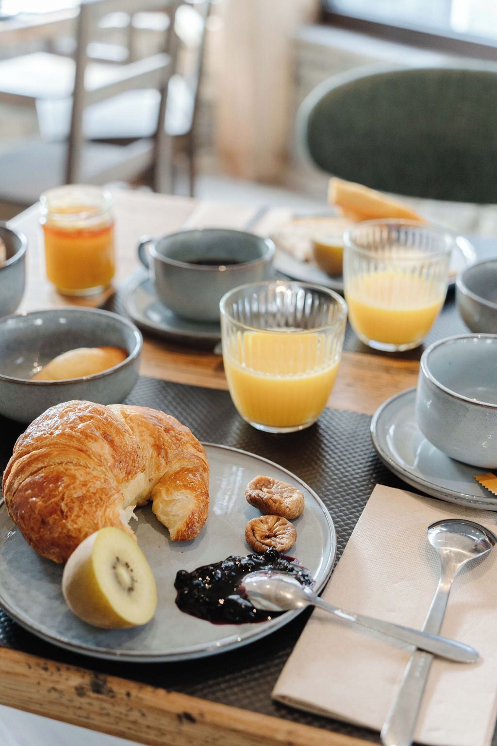 Desayuno con cruasanes, fruta y jugo sobre una mesa.