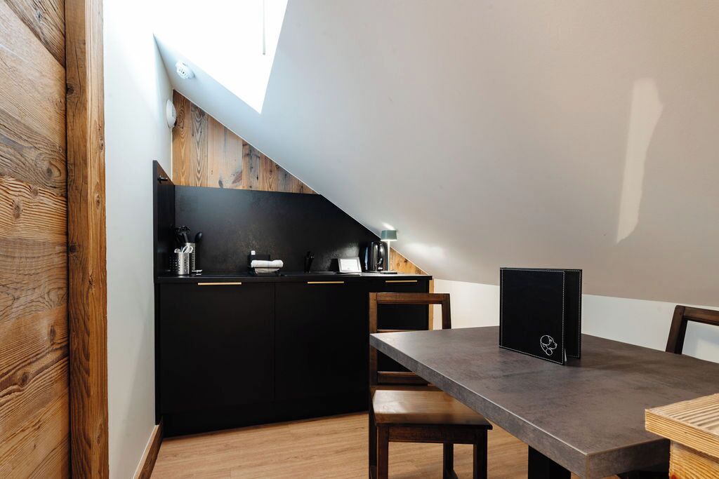 A modern kitchen with a black countertop, wooden cabinets, and a dining area with a table and chairs.