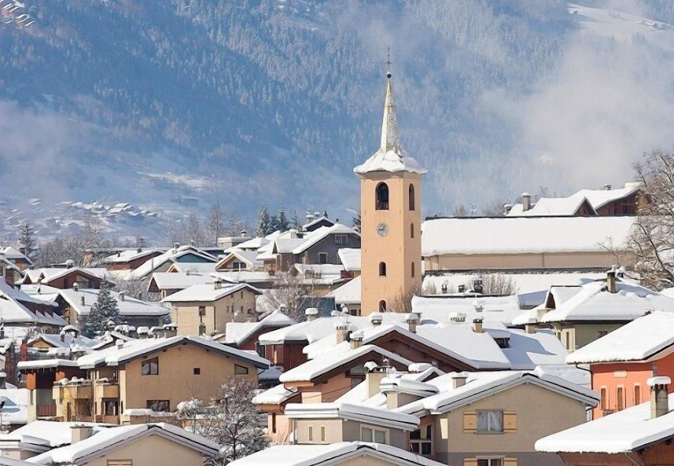 A snow-covered village with a prominent church tower and residential buildings.