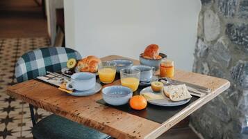 A breakfast setting with a wooden table, a checkered chair, and a stone wall in the background.
