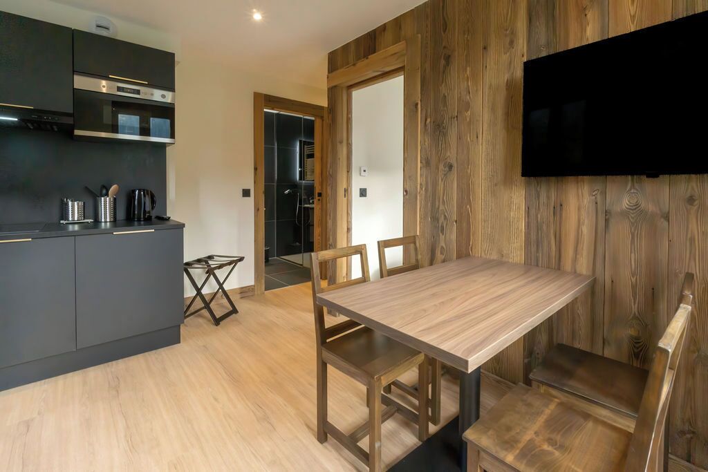 Una cocina moderna con armarios oscuros, una mesa de comedor de madera y un televisor montado en una pared de madera.