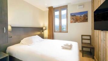 Quarto de hotel com cama, mesa de cabeceira, janela com cortinas, televisão na parede e um quadro.