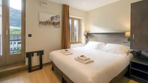 Habitación de hotel con una cama grande, vistas a las montañas a través de la ventana, un cuadro en la pared y un televisor al lado.