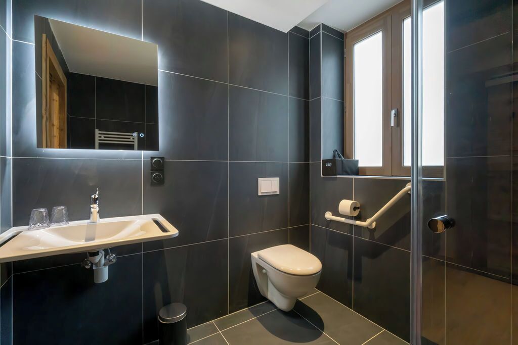 Une salle de bain moderne avec des carreaux foncés, un lavabo blanc, des toilettes et une douche en verre.