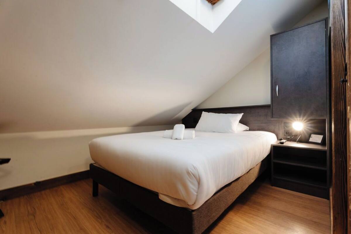 A bedroom with a bed, a nightstand, a wardrobe, and a skylight.