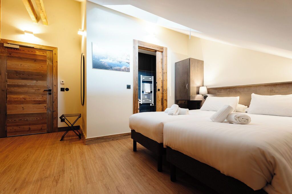 Une chambre d’hôtel avec une porte en bois, un lit avec du linge de maison blanc, une table de chevet et un radiateur fixé au mur.