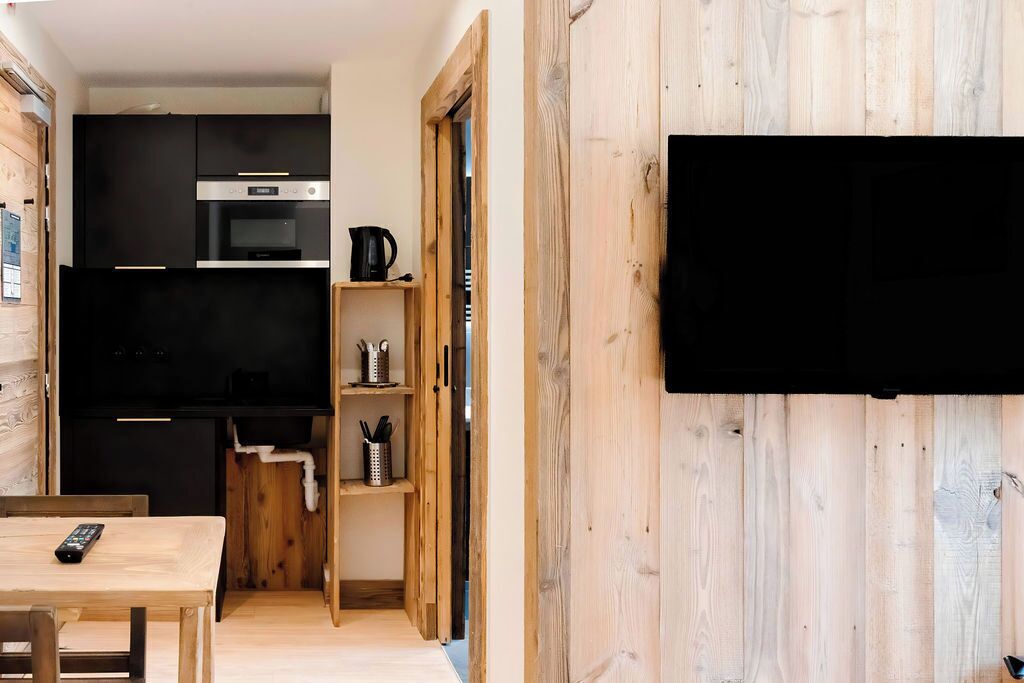 A compact kitchen with modern appliances, a wooden dining area, and a flat-screen TV mounted on the wall.