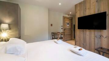 A hotel room with a bed, a desk, a chair, a TV mounted on the wall, and a wooden panel wall.