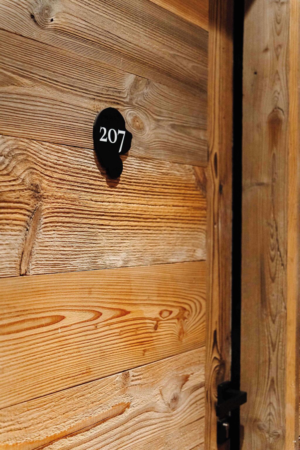 A wooden door with a black number plate displaying '207'.