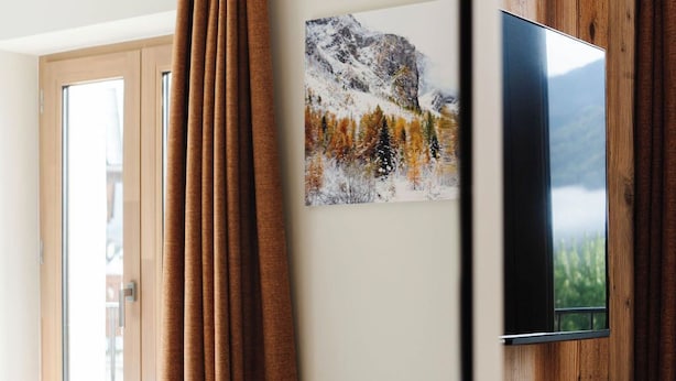 Una habitación de hotel con cama, televisión montada en una pared de madera y ventana con cortinas.