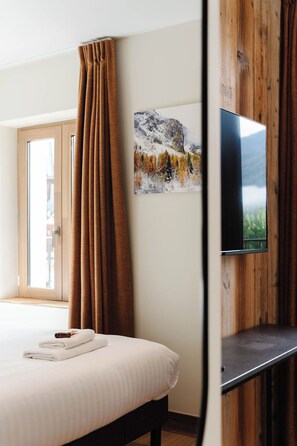 A hotel room with a bed, a TV mounted on a wooden wall, and a window with curtains. - Hostellerie du petit Saint Bernard (Bourg-Saint-Maurice)