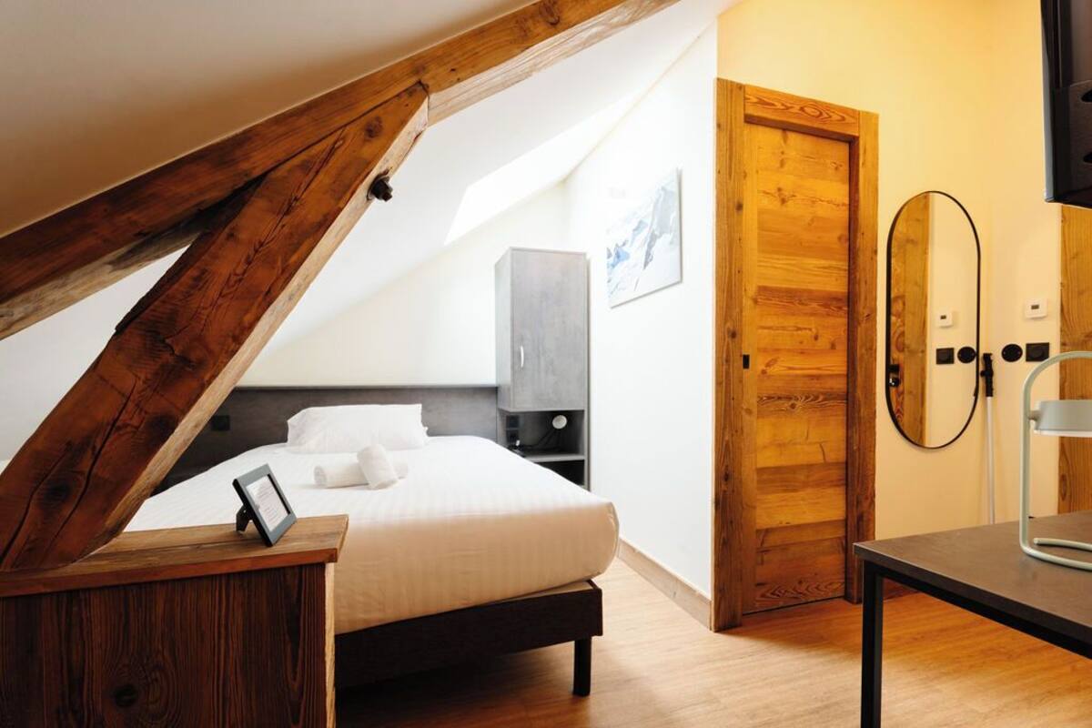 A bedroom with a wooden ceiling, a bed, a bedside table, a wardrobe, and a door.