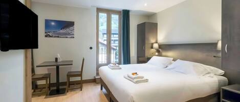 Een hotelkamer met een bed, een bureau, een stoel, een televisie en een raam met uitzicht.