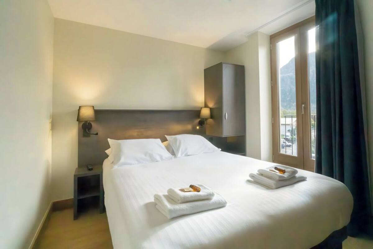 A hotel room with a large bed, two bedside tables, a wardrobe, and a window with curtains.
