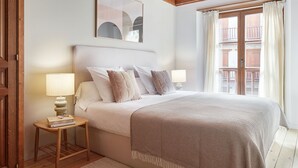 A bedroom with a large bed, two bedside lamps, a small table with a book, and a window with curtains. - Val de Ruda Luxe 10 by FeelFree Rentals (Baqueira)