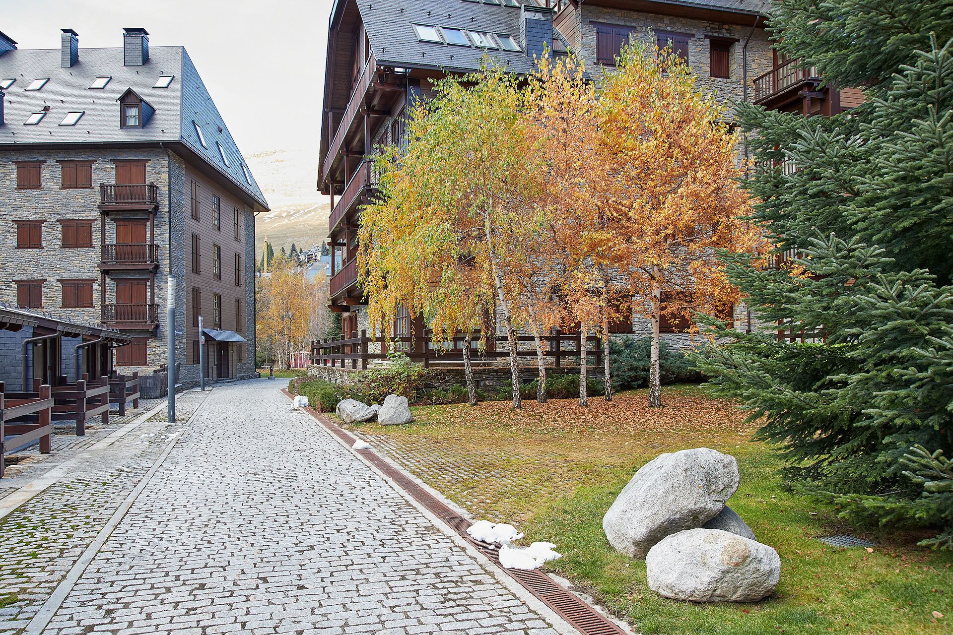 Eine Kopfsteinpflasterstraße gesäumt von traditionellen Steinbauten, einem Holzzaun und Herbstbäumen.
