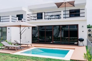 Ein modernes, zweistöckiges Haus mit Swimmingpool, Sitzgelegenheiten im Freien und Grillplatz.