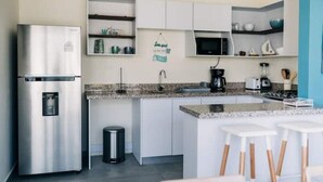 A modern kitchen with a stainless steel refrigerator, white cabinets, a granite countertop, and a small island with bar stools. - NEW Bayfront Villa in Costa del Sol

 (El Zapote)