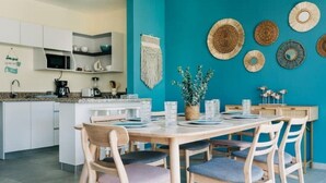 A modern kitchen with white cabinets, a teal accent wall, and a dining area with wooden chairs and a table set for four. - NEW Bayfront Villa in Costa del Sol

 (El Zapote)