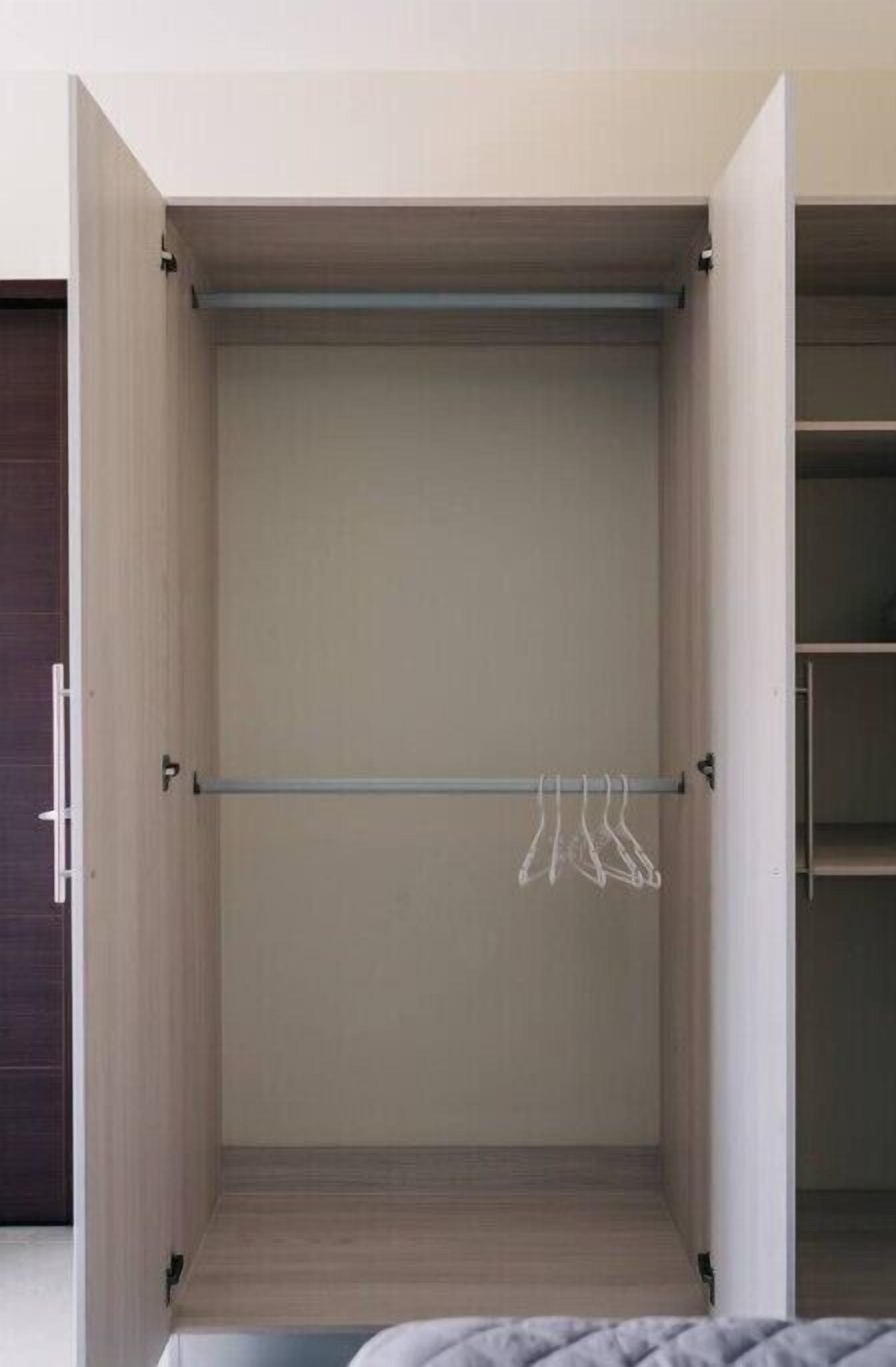 A walk-in closet with a metal rod for hanging clothes, wooden flooring, and a dark-colored door.