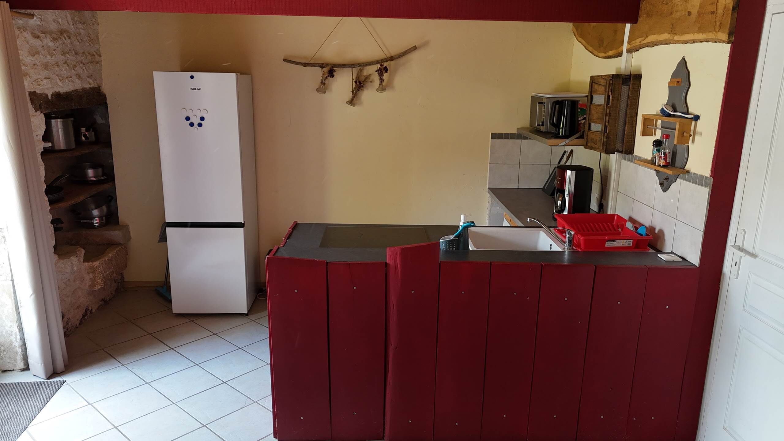 A compact kitchen with a refrigerator, a wooden shelf, and a red counter.
