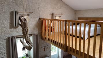 A room with a loft bed, a wooden railing, and a rustic decor including a hanging light fixture.
