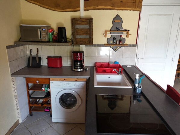 A compact kitchen with a washing machine, a coffee maker, and a sink. - Gite Comme A La Maison (MONTILS)