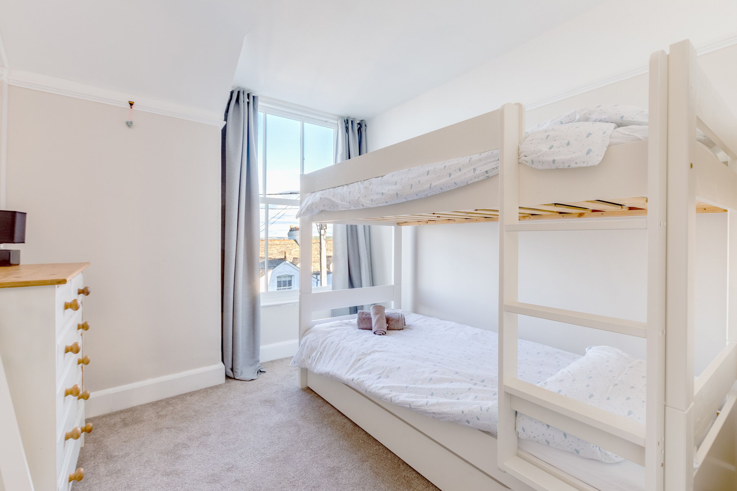 A bunk bed room with a window, a dresser, and a desk.