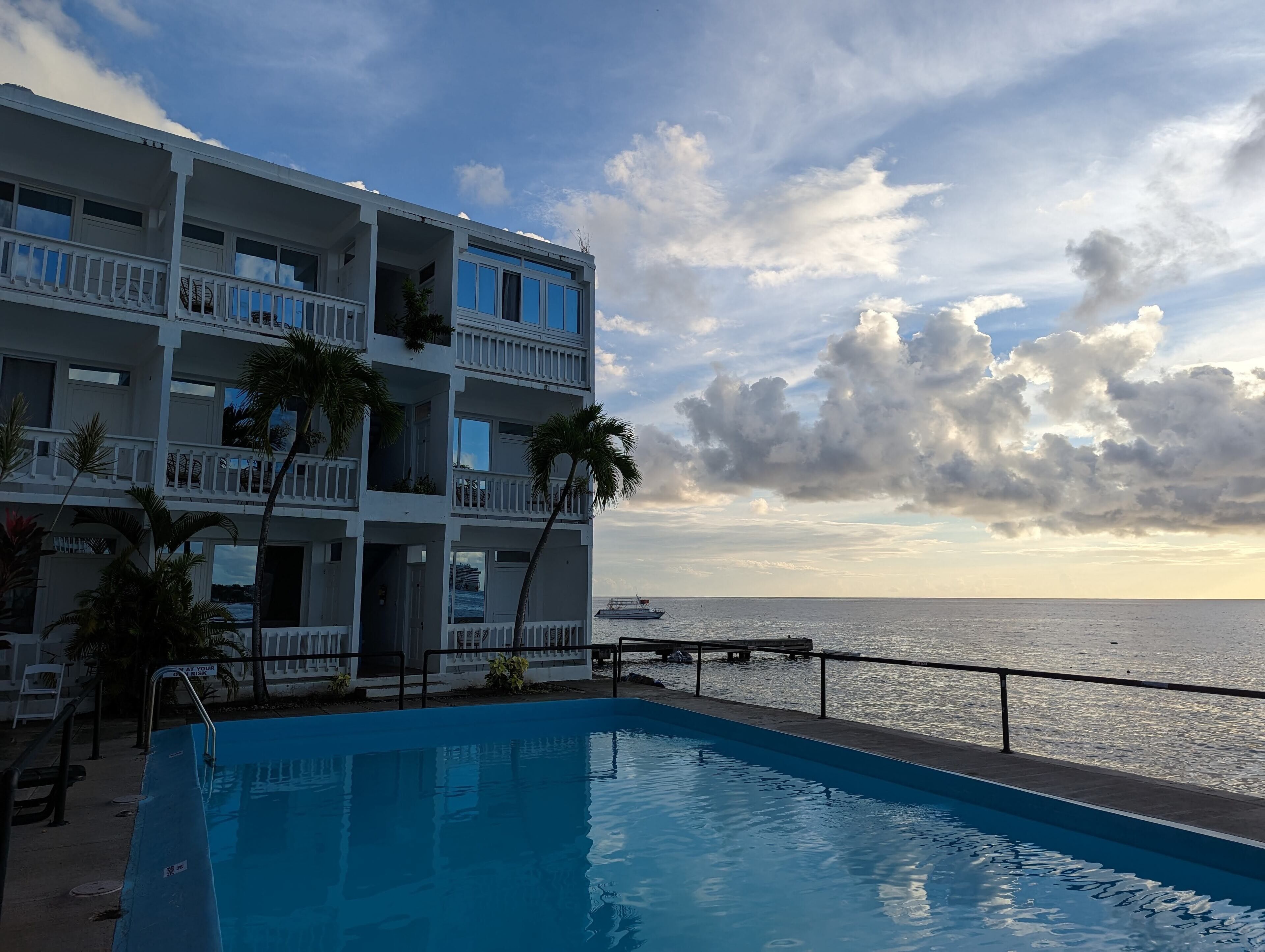 Ein Hotel mit Pool, Meerblick und einem Balkon mit Palmen.