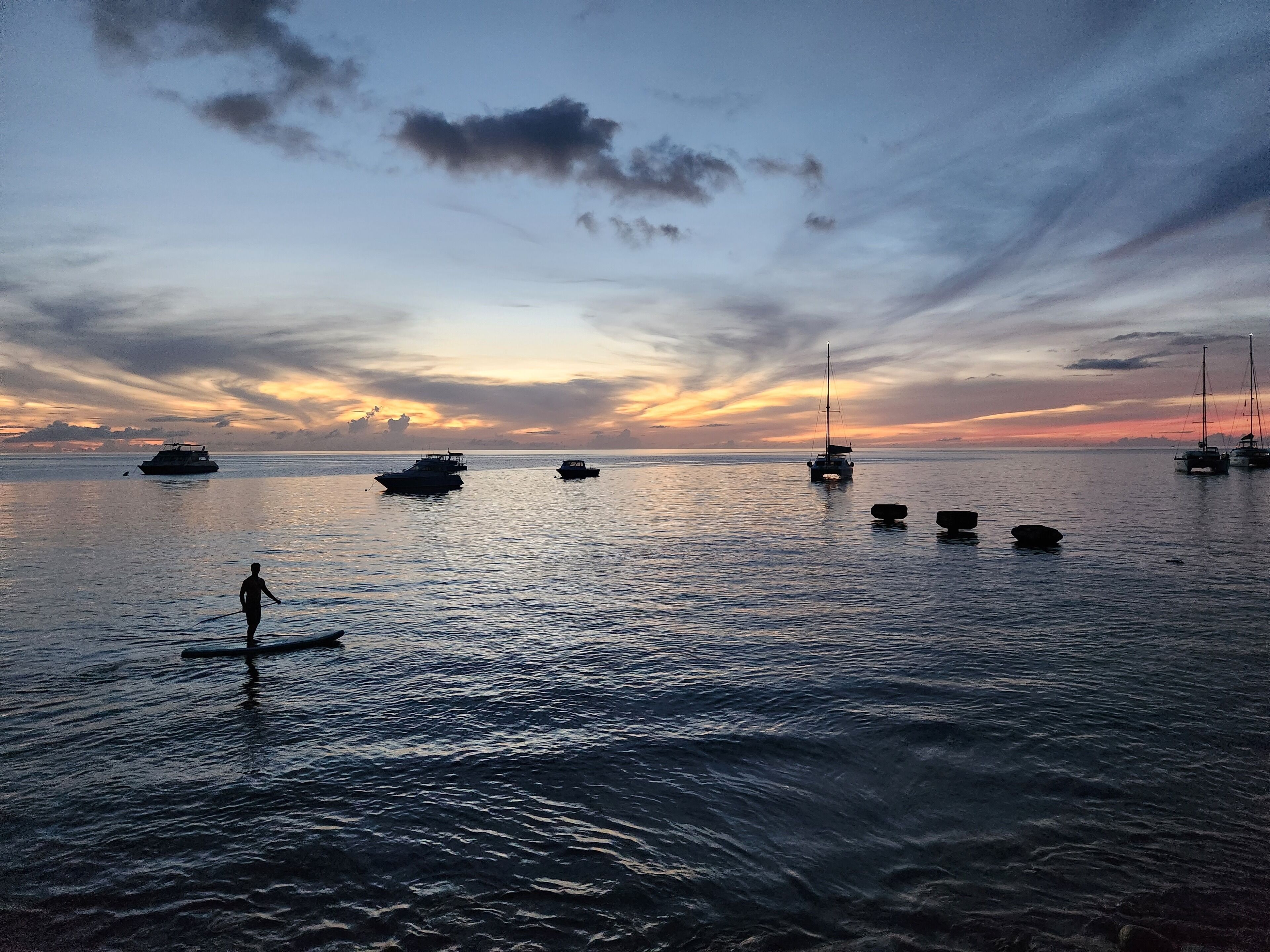A calm sea with several boats and a person paddleboarding.
