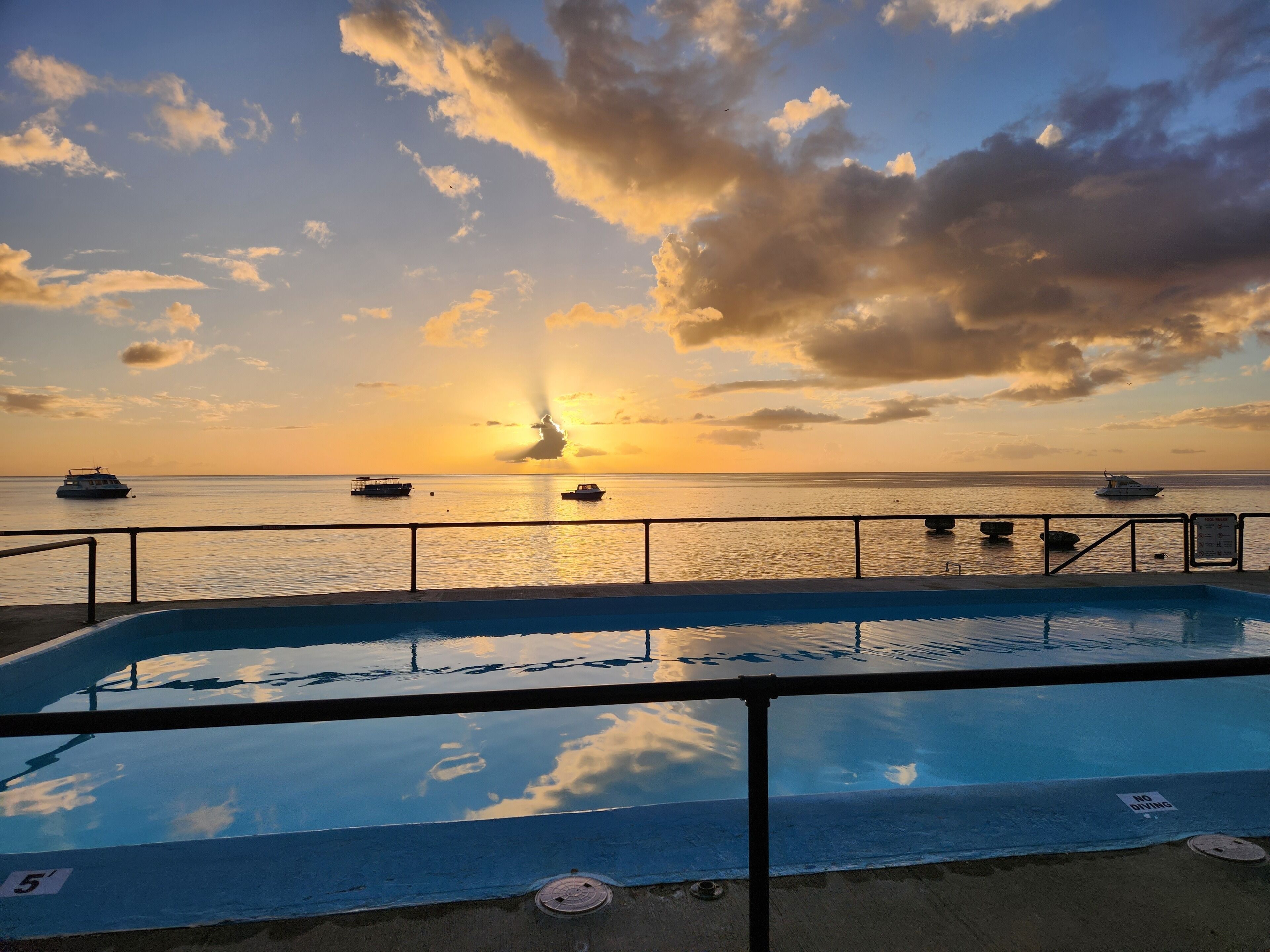 A pool with a view of boats on the water during sunset.
