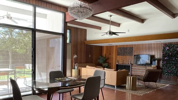 A spacious living room with a glass dining table, modern chairs, a ceiling fan, and a large window. - Beautiful botanical themed 4 bedroom home in historical downtown neighborhood  (Las Vegas)