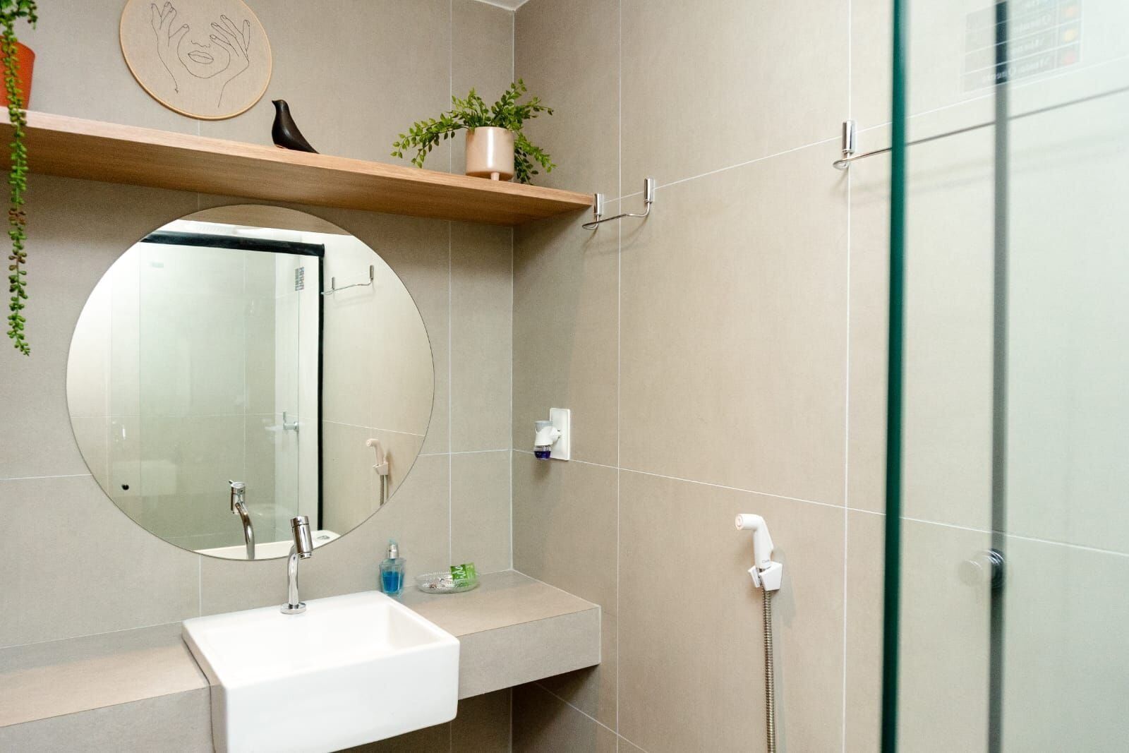 Un baño moderno con un espejo redondo, un lavamanos blanco, un cabezal de ducha de mano y un box de ducha con paredes de vidrio.