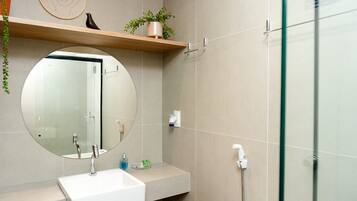 Un baño moderno con un espejo redondo, un lavamanos blanco, un cabezal de ducha de mano y un box de ducha con paredes de vidrio.