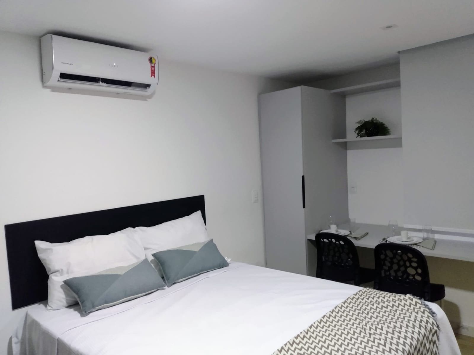 Quarto de hotel com cama, escrivaninha e ar condicionado.