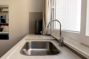 Una cocina moderna con un lavamanos de acero inoxidable, horno empotrado y una ventana con cortinas.