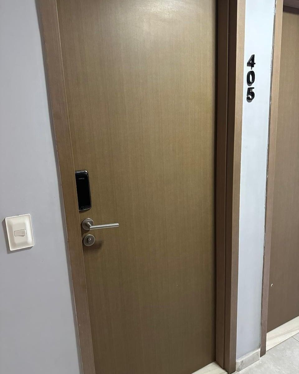 Una puerta cerrada con teclado numérico, un interruptor de luz en la pared y el número '405' en la pared contigua.