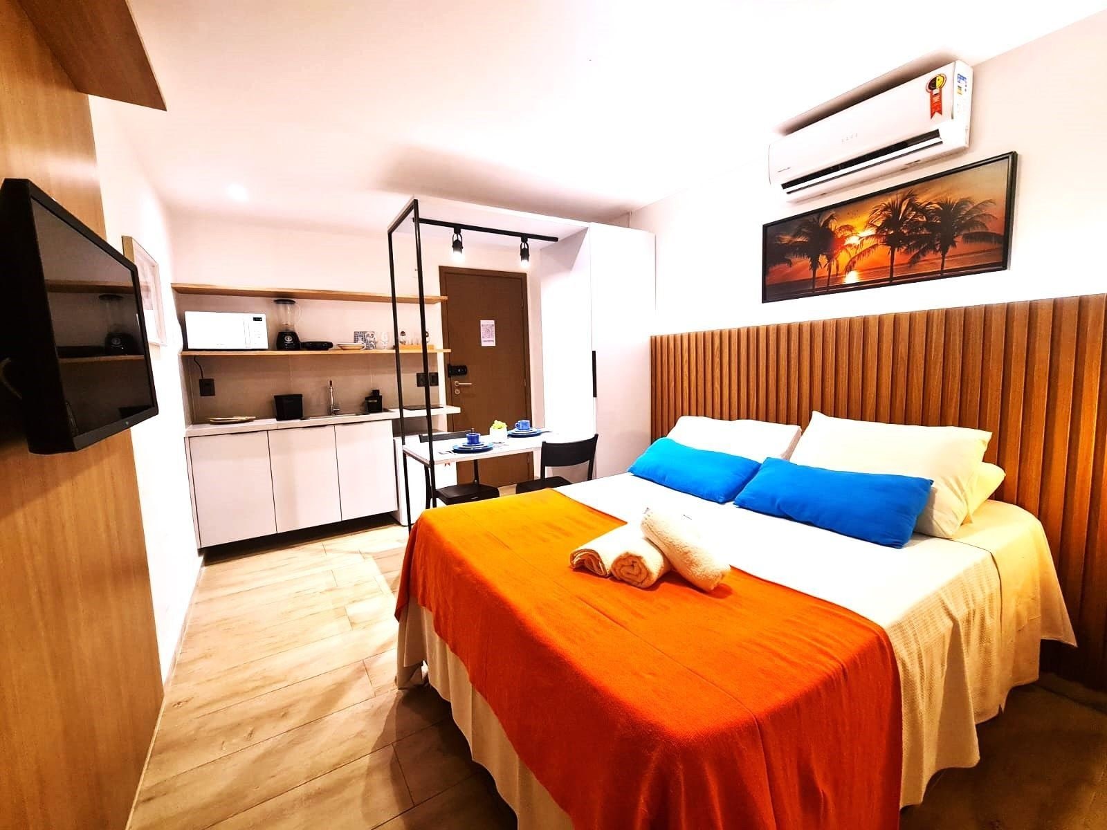Una habitación de hotel con cama, televisión, kitchenette y aire acondicionado.