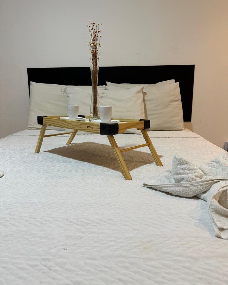 A neatly made bed with a wooden bedside table, a vase with dried flowers, and a white towel on the bed.
