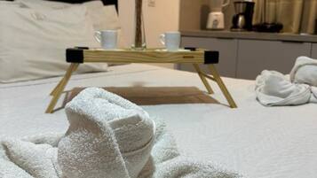 Una cama bien hecha con un albornoz blanco, una mesita de noche con una taza y un florero, y una cafetera en la mesita auxiliar.