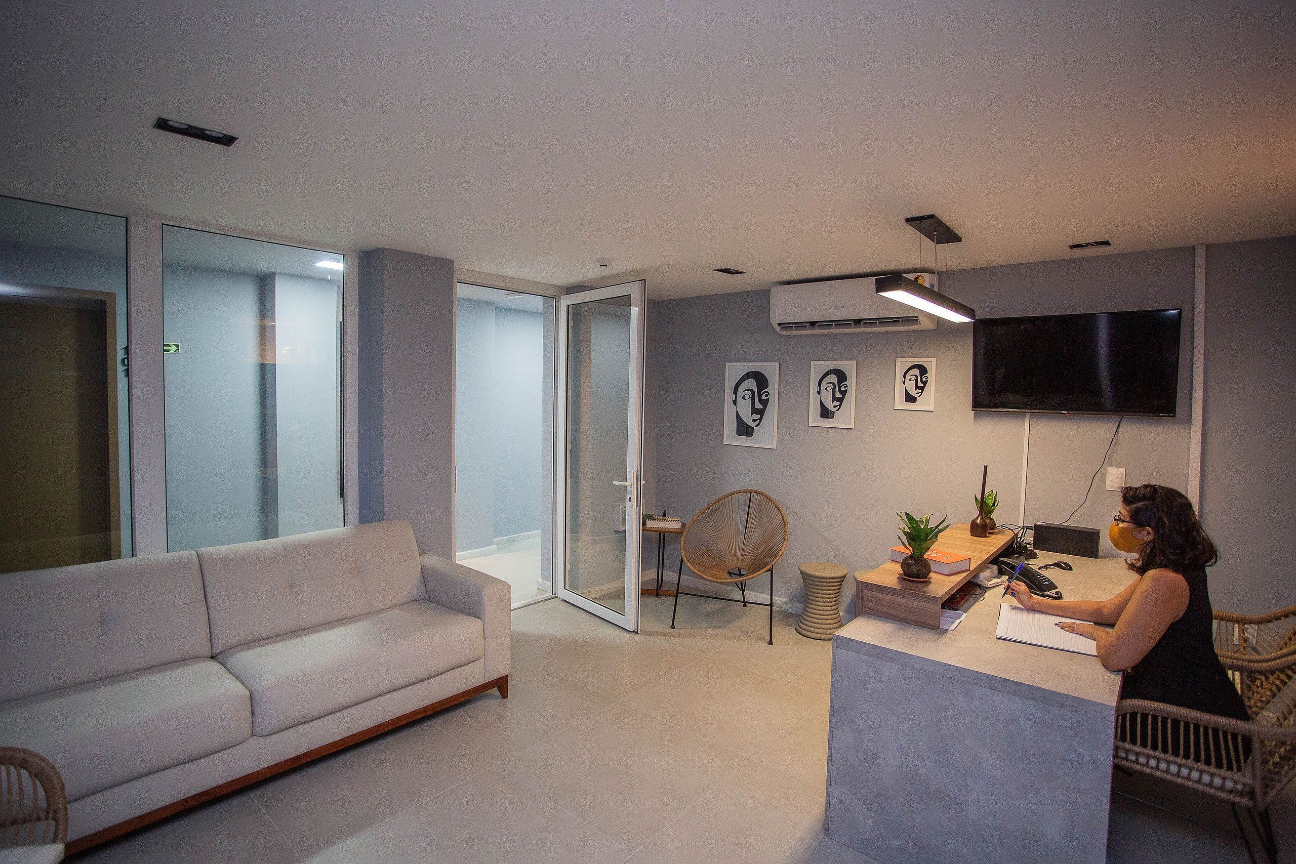 A modern living room with a sofa, a dining area with a table and chairs, a TV mounted on the wall, and a glass door leading to another room.